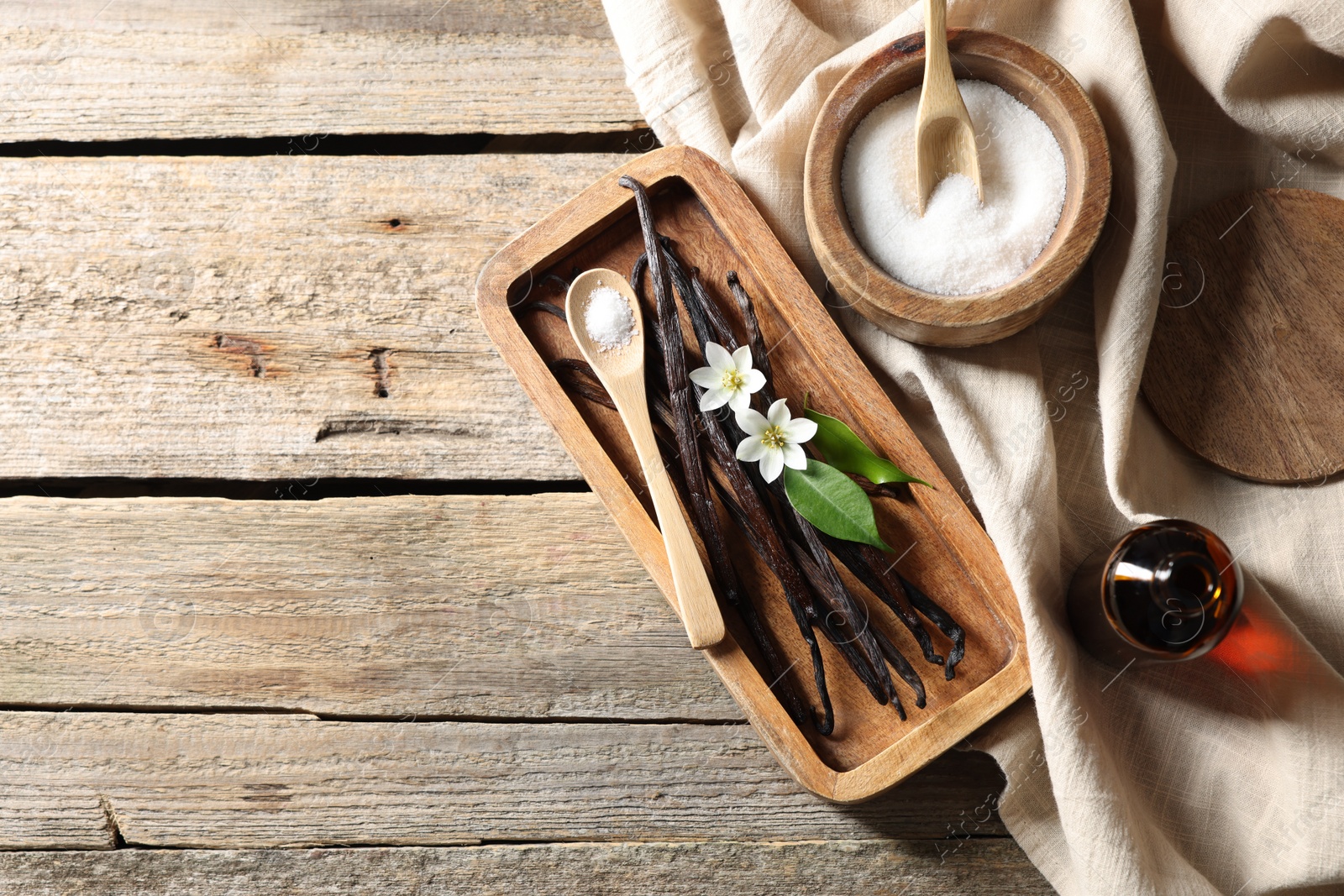 Photo of Vanilla pods, flowers, leaves and sugar on wooden table, top view. Space for text