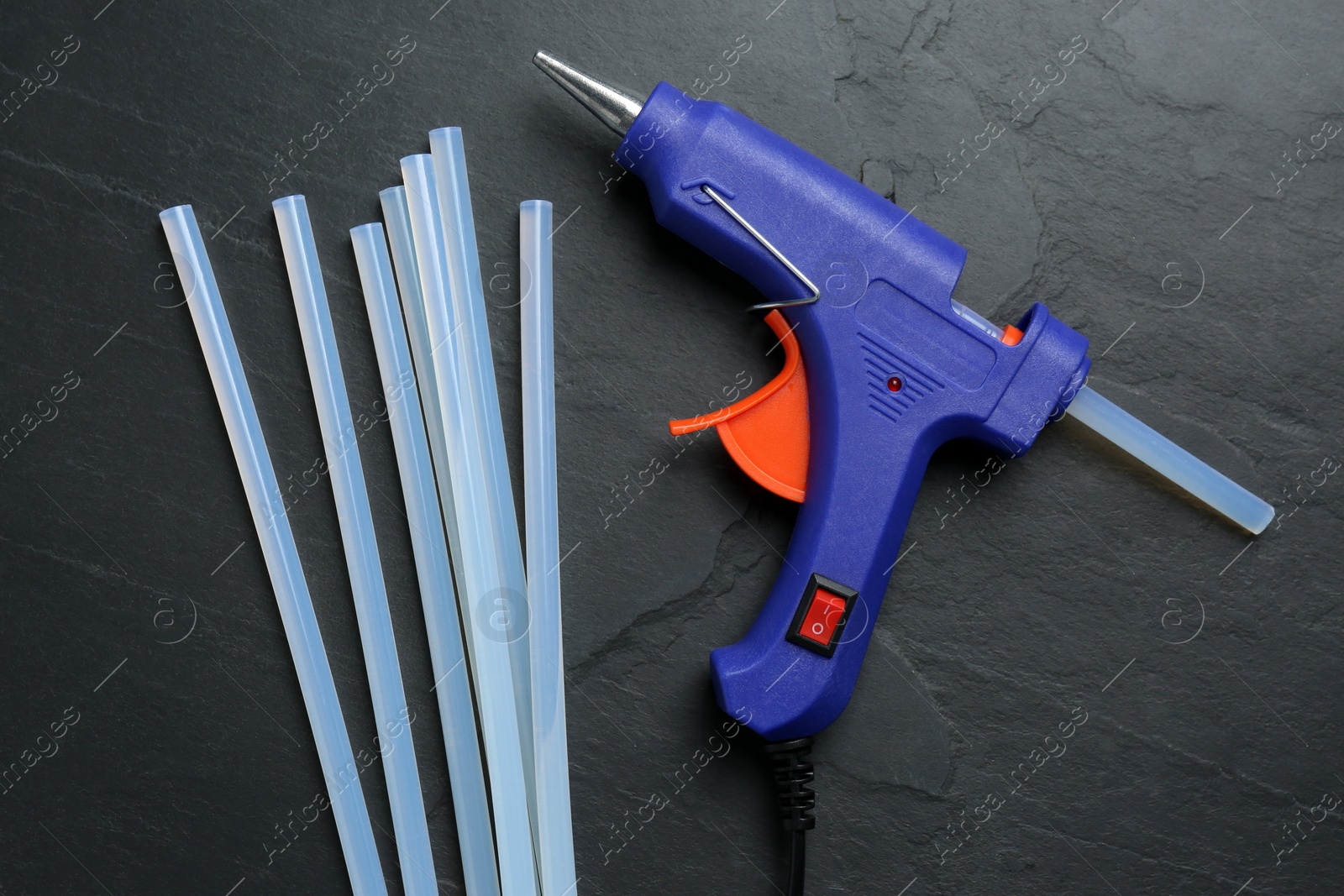 Photo of Blue glue gun and sticks on black table, flat lay