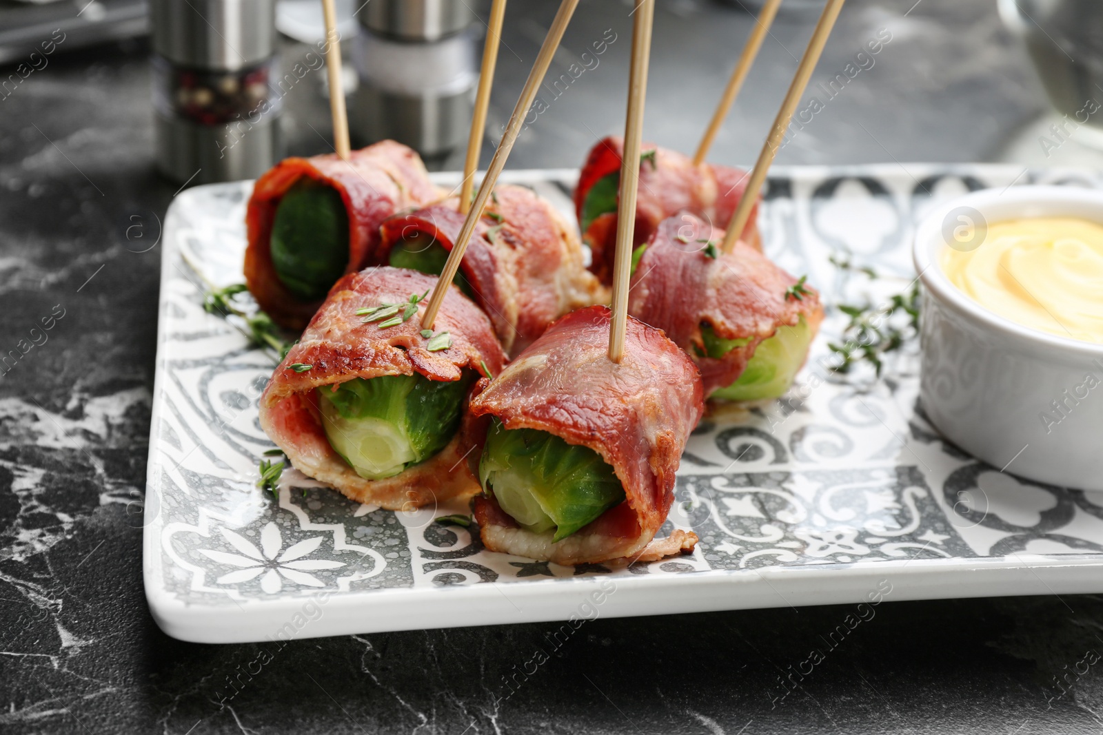 Photo of Plate with Brussels sprouts wrapped in bacon on marble table, closeup