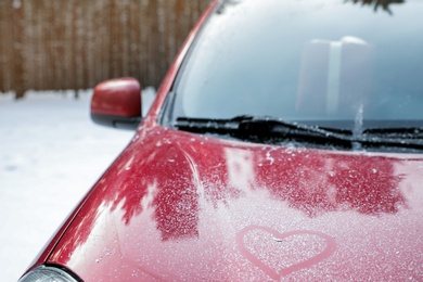 Modern car with drawn heart on hood in snowy winter forest, closeup. Space for text
