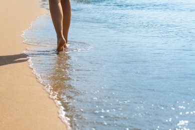 Photo of Woman walking through water on seashore, closeup of legs