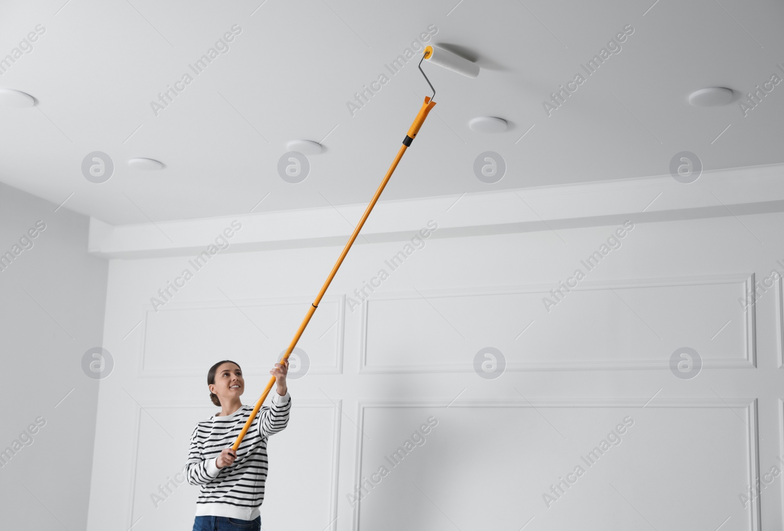 Photo of Young woman painting ceiling with white dye indoors, space for text