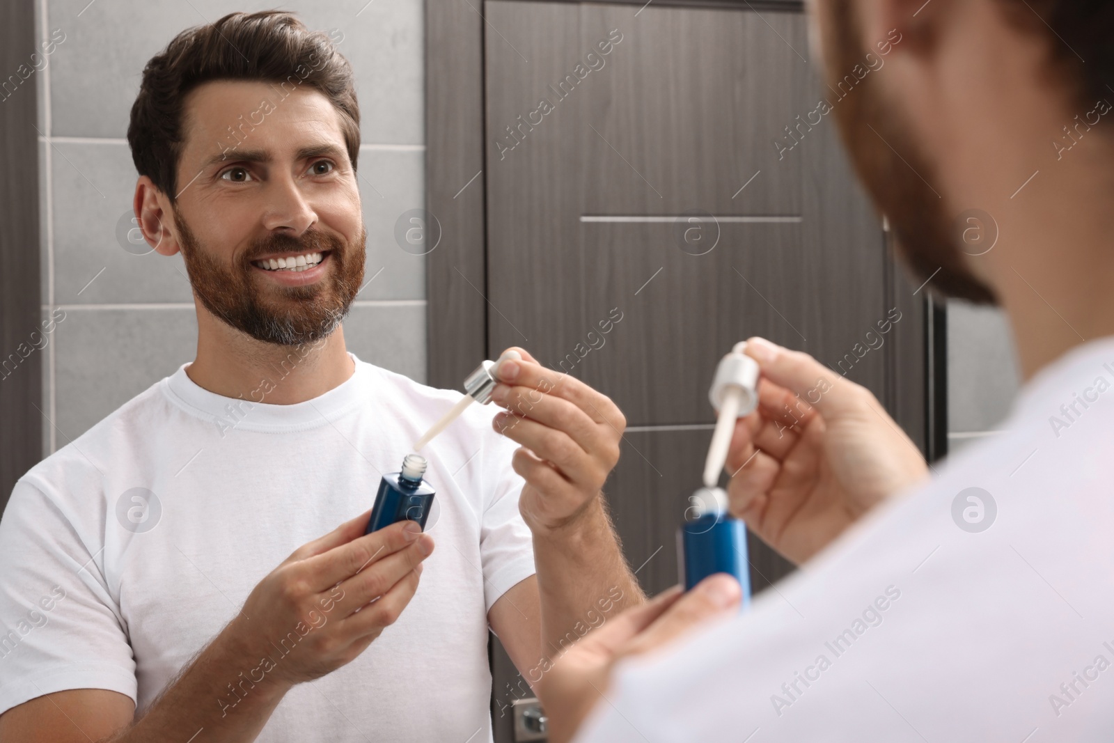 Photo of Handsome bearded man with bottle of oil in bathroom