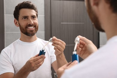 Photo of Handsome bearded man with bottleoil in bathroom