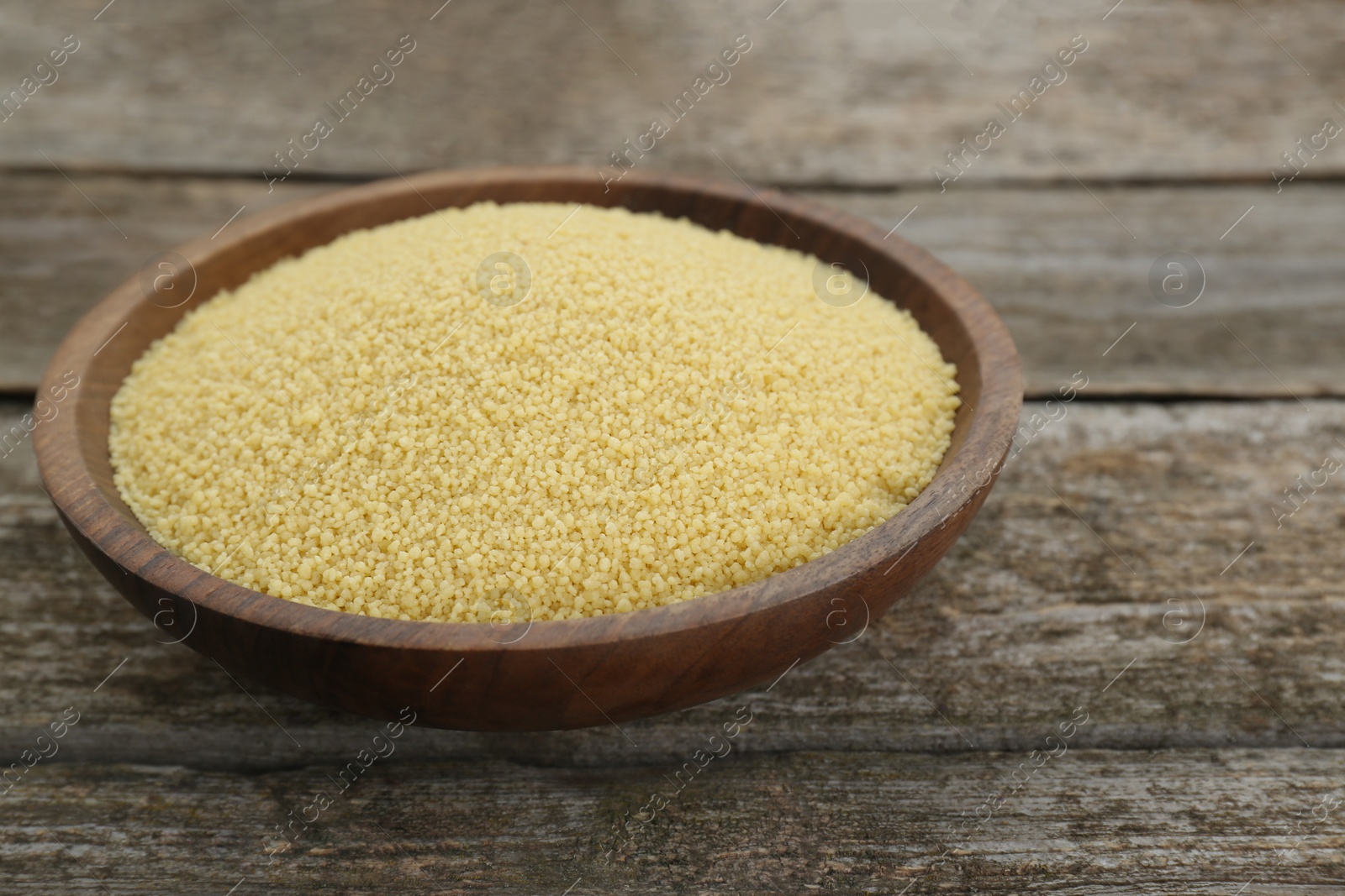 Photo of Bowl of raw couscous on wooden table, closeup