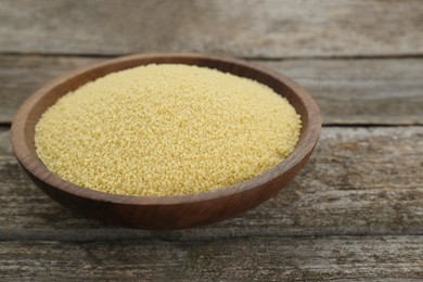 Bowl of raw couscous on wooden table, closeup