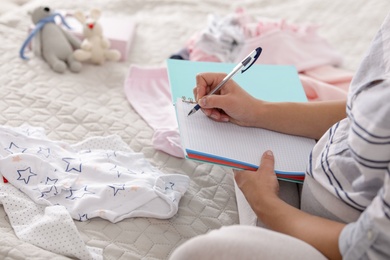 Photo of Pregnant woman writing packing list for maternity hospital on bed at home, closeup