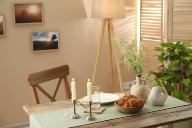 Photo of Clean tableware, candlesticks, flowers and fresh pastries on table in stylish dining room