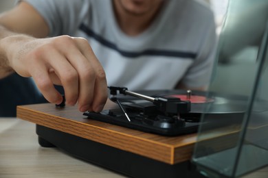 Man using turntable at wooden table indoors, closeup