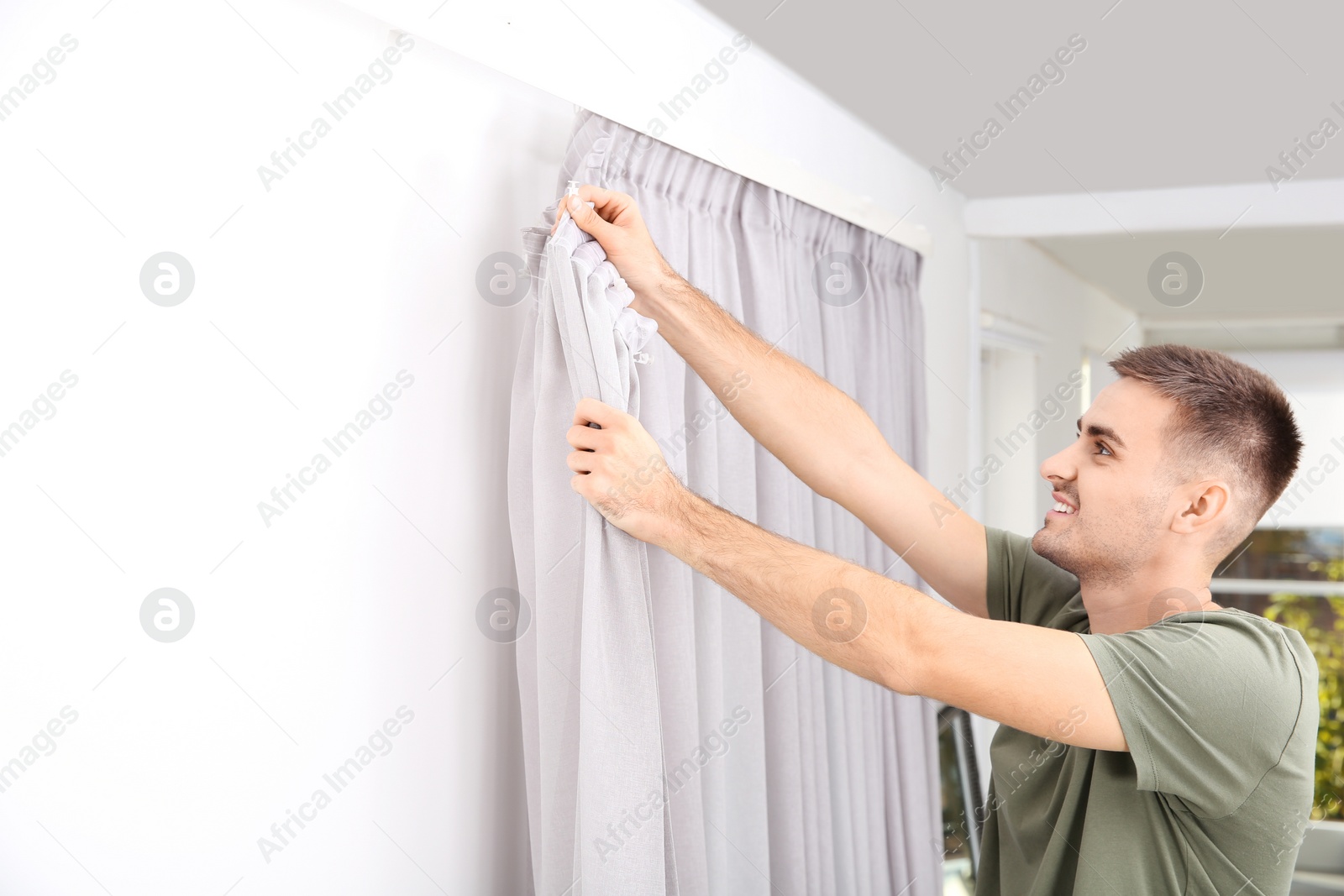 Photo of Man hanging window curtain indoors. Interior decor element