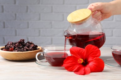 Woman pouring delicious hibiscus tea into cup at light wooden table, closeup