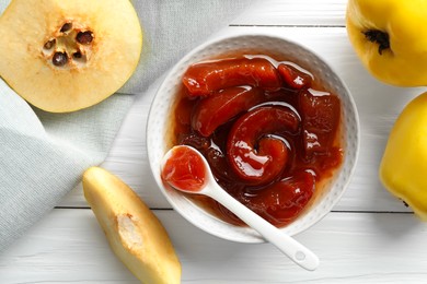 Photo of Tasty homemade quince jam in bowl, spoon and fruits on white wooden table, flat lay