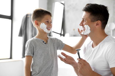 Son applying shaving foam onto father's face in bathroom