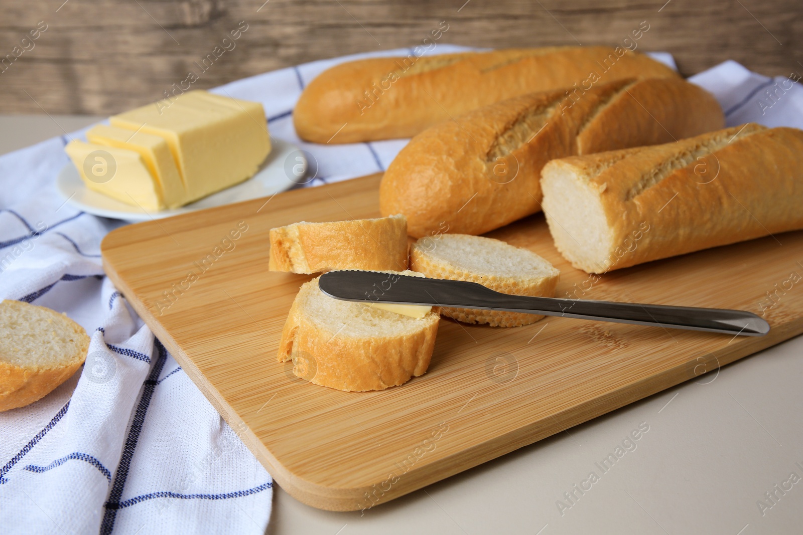 Photo of Tasty cut baguette with fresh butter on white table