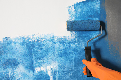 Photo of Woman painting white wall with blue dye, closeup