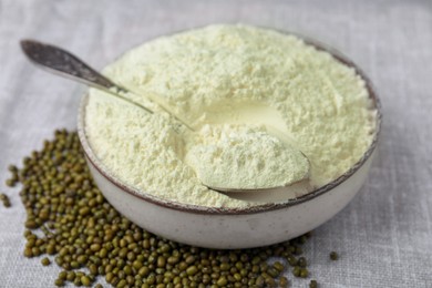 Photo of Bowl of flour, spoon and mung beans on light grey cloth, closeup