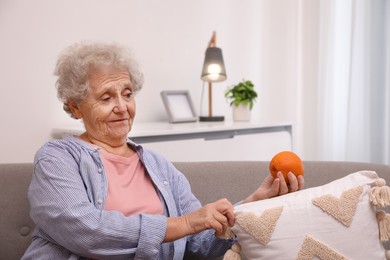 Photo of Senior woman finding orange on sofa home. Age-related memory impairment