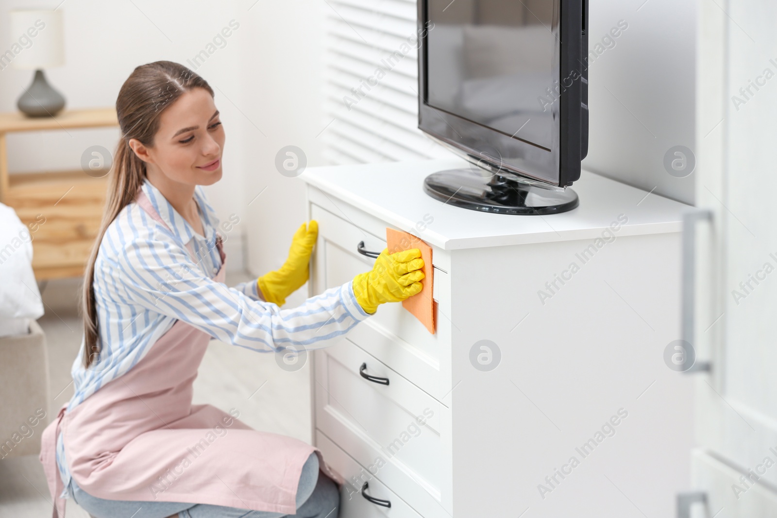 Photo of Young chambermaid wiping dust from furniture in hotel room