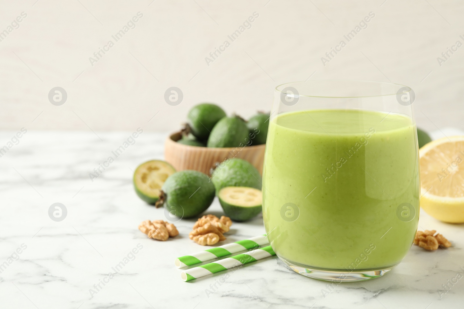 Photo of Fresh feijoa smoothie in glass on white marble table, closeup. Space for text