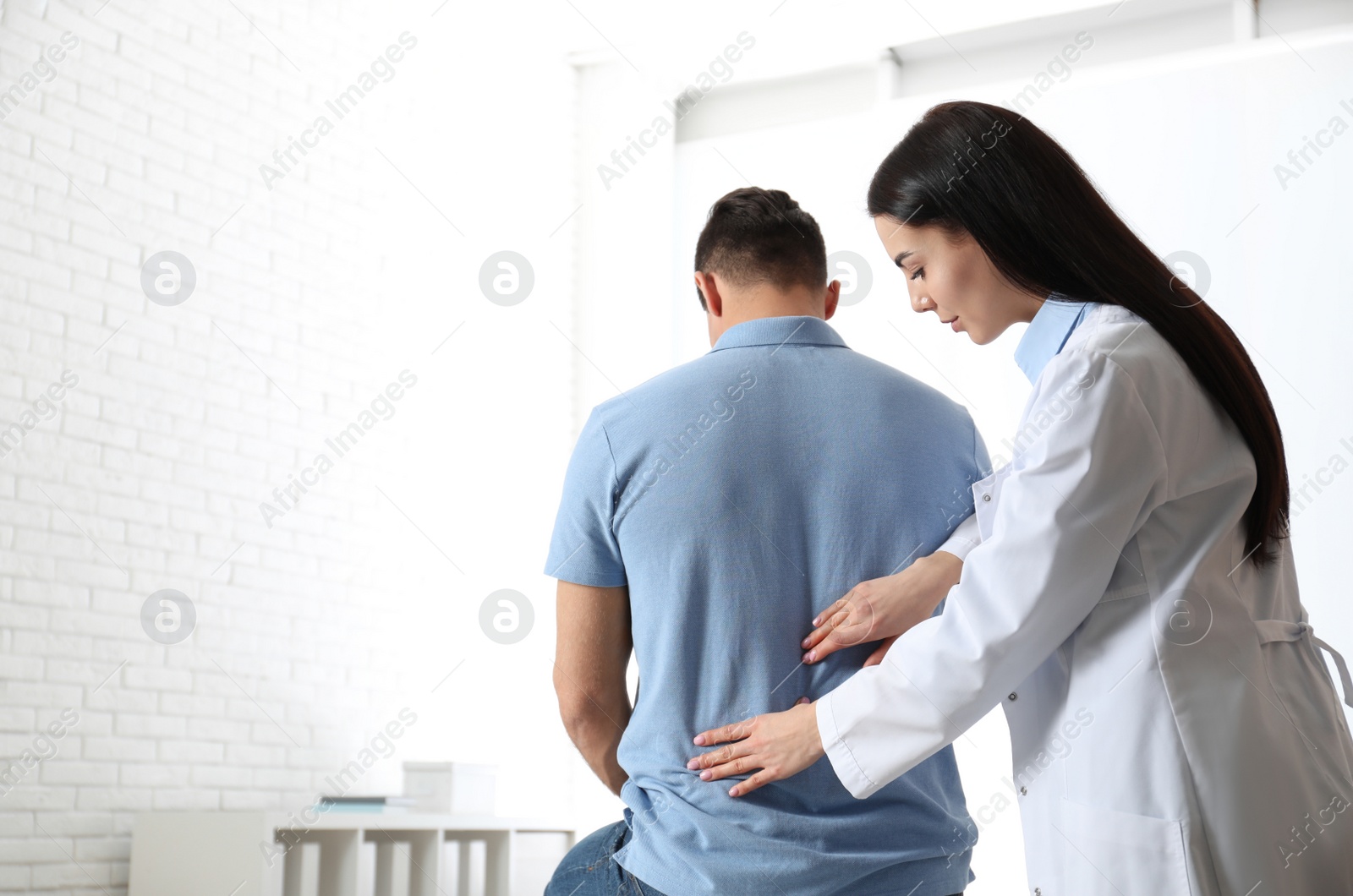 Photo of Professional orthopedist examining man in medical office. Space for text