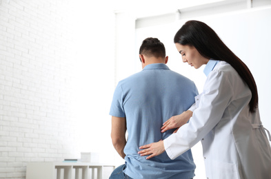 Professional orthopedist examining man in medical office. Space for text