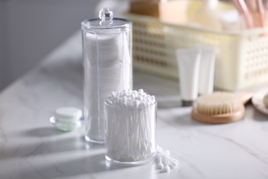Photo of Cotton buds and pads in transparent holders on white marble table