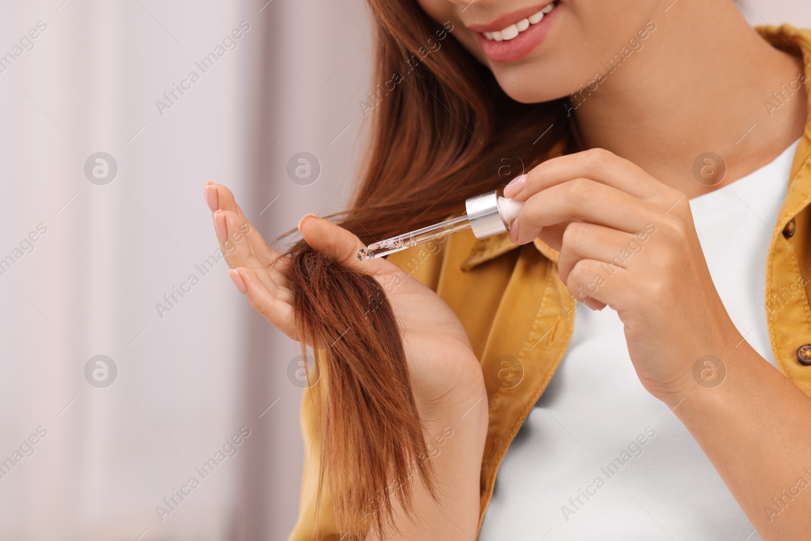 Photo of Woman applying serum onto hair indoors, closeup