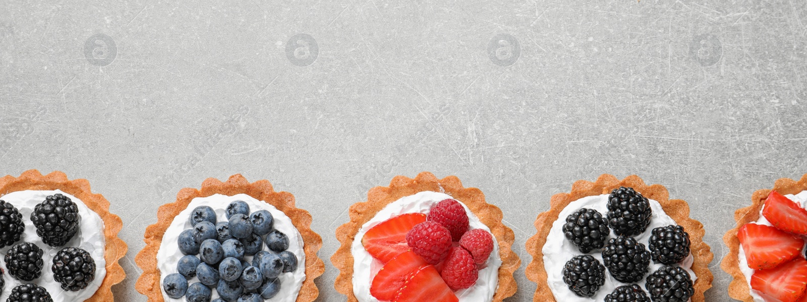 Image of Delicious tartlets with fresh berries on light grey table, flat lay with space for text. Banner design