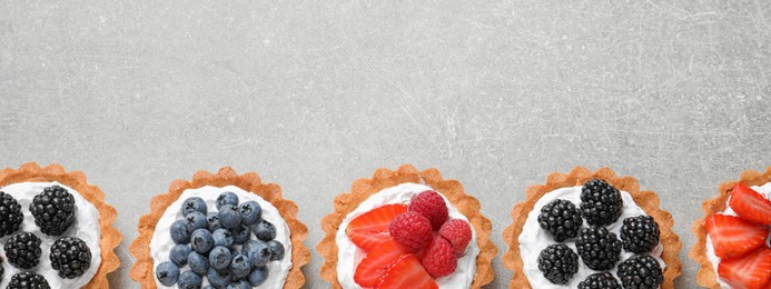 Image of Delicious tartlets with fresh berries on light grey table, flat lay with space for text. Banner design