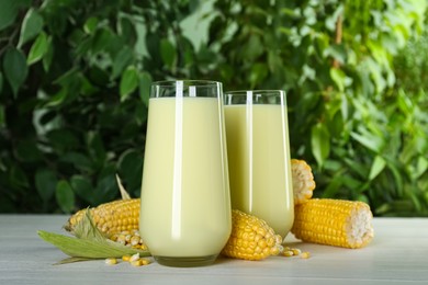 Photo of Tasty fresh corn milk and cobs on light table against blurred background