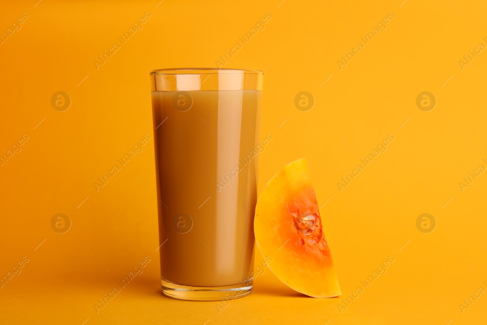 Photo of Tasty pumpkin juice in glass and cut pumpkin on orange background