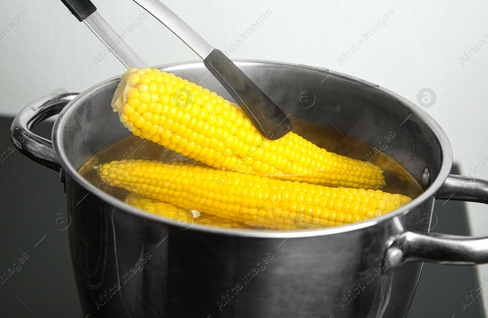 Photo of Taking fresh corn cob from pot with hot water on stove