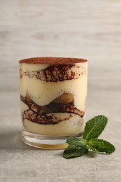 Delicious tiramisu in glass and mint on grey textured table, closeup