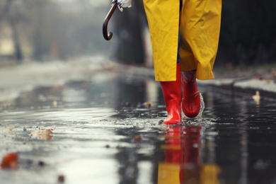 Photo of Woman in rubber boots walking outdoors on rainy day, closeup. Space for text