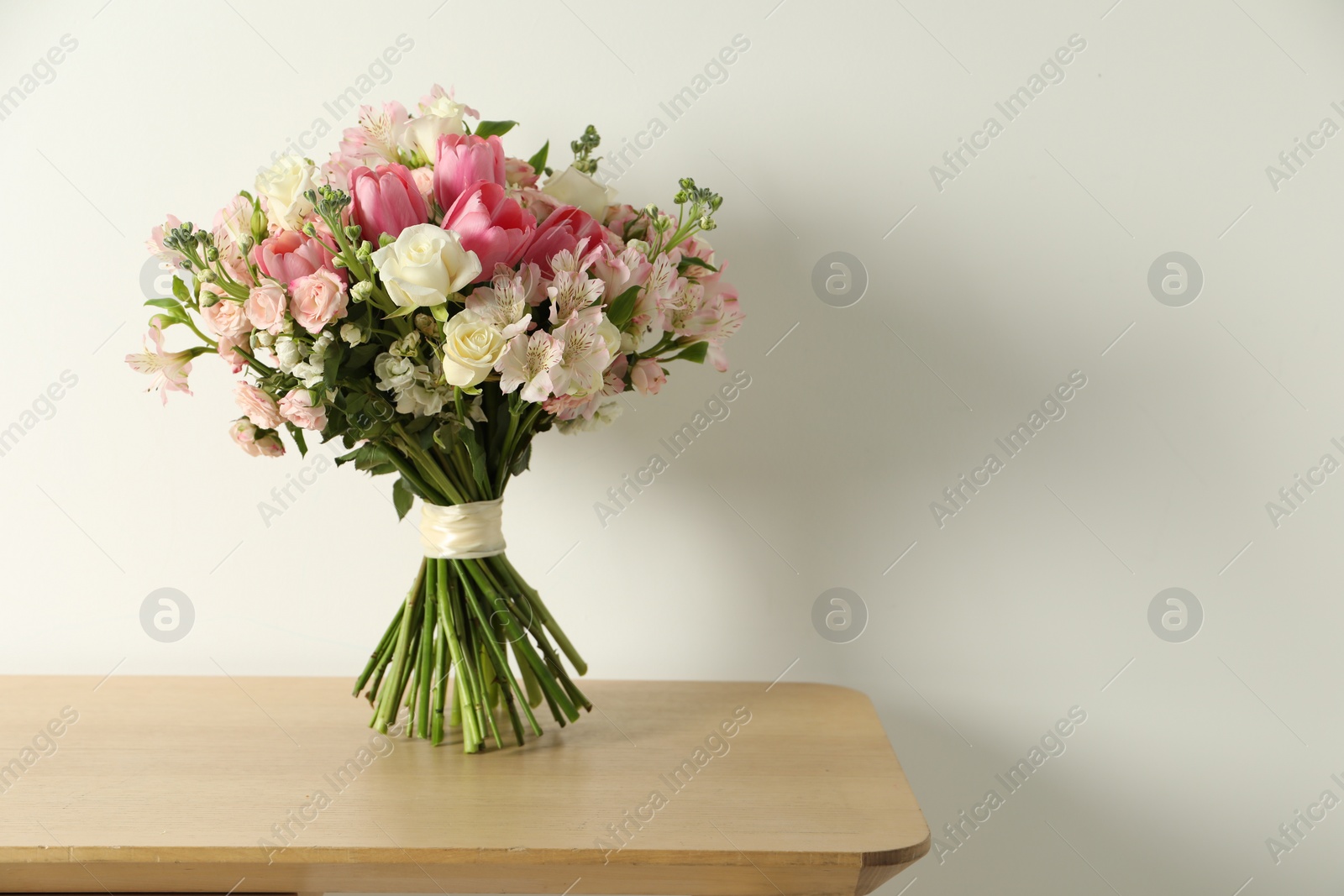 Photo of Beautiful bouquet of fresh flowers on wooden table near light wall. Space for text