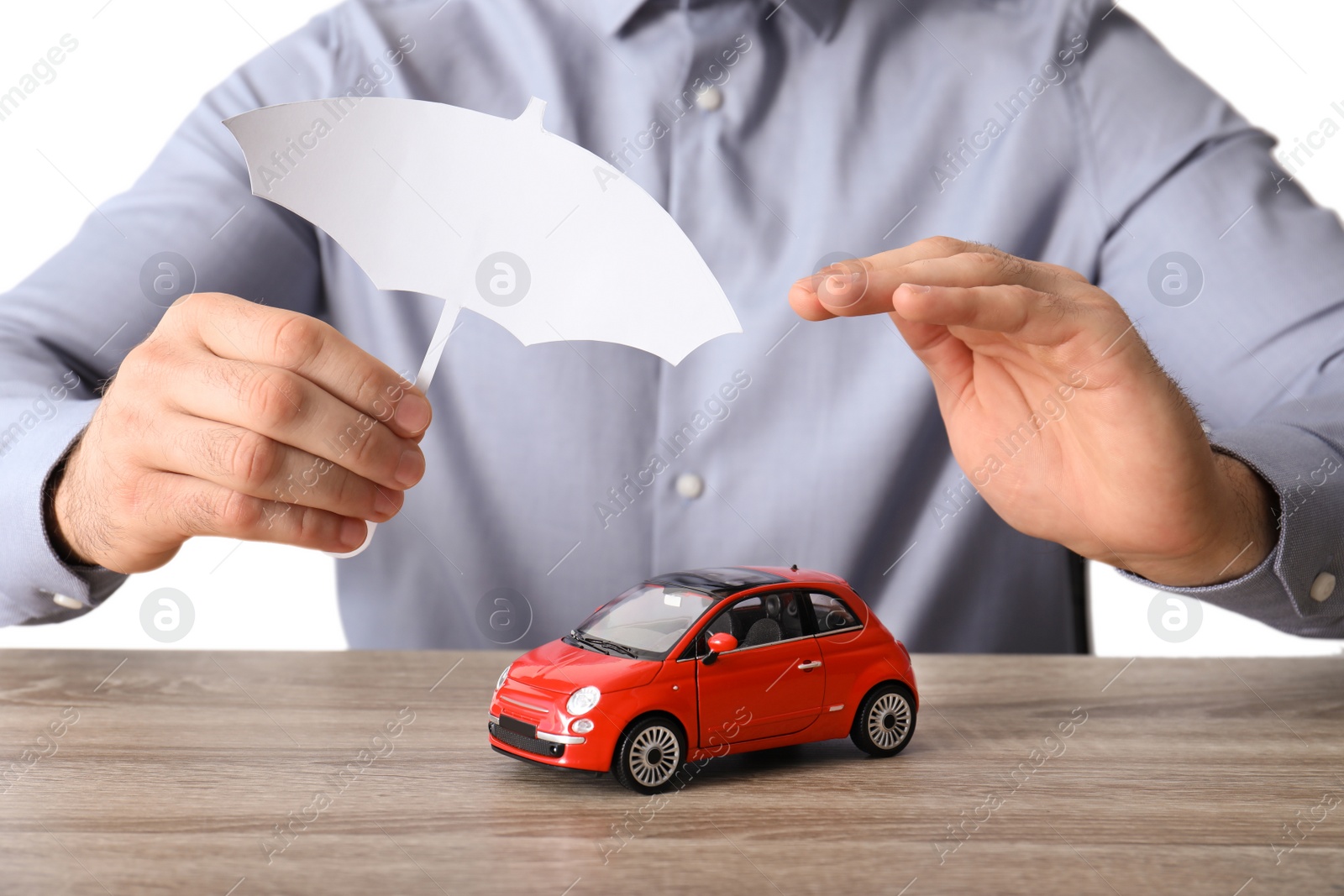 Photo of Male insurance agent covering toy car with paper cutout umbrella and hand at table, closeup