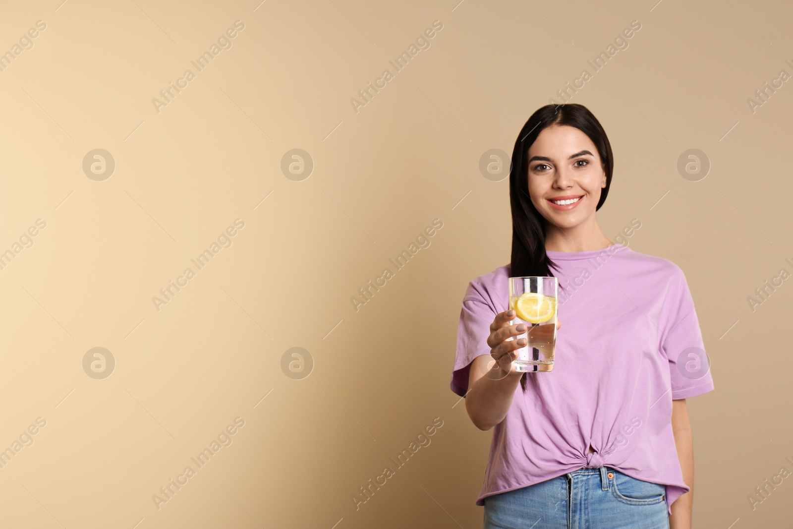 Photo of Beautiful young woman with tasty lemon water on beige background. Space for text