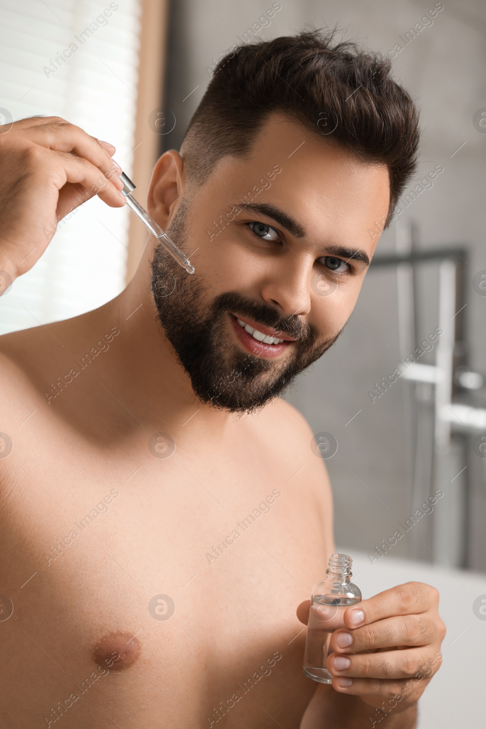 Photo of Handsome man applying cosmetic serum onto his face in bathroom