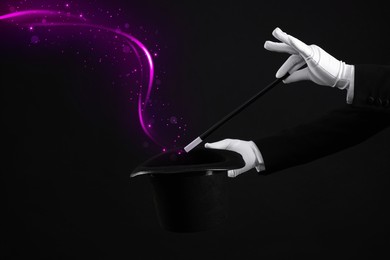 Image of Magician showing trick with wand and top hat on black background, closeup