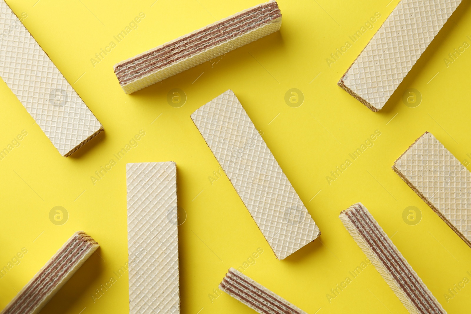 Photo of Tasty wafer sticks on yellow background, flat lay. Sweet food