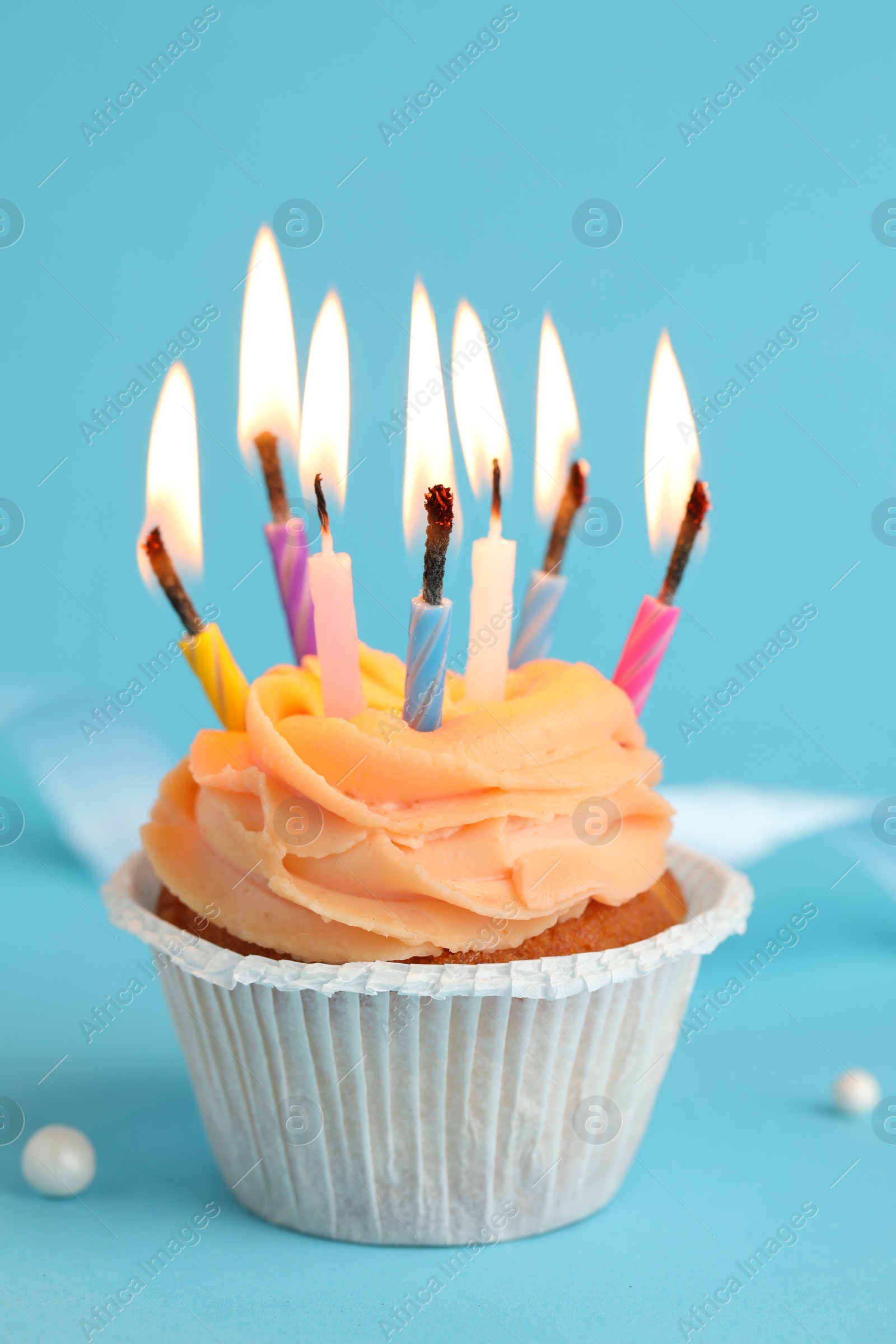 Photo of Tasty birthday cupcake with many candles on light blue background, closeup