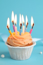 Tasty birthday cupcake with many candles on light blue background, closeup