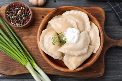 Photo of Bowl of tasty dumplings served on dark wooden table, flat lay