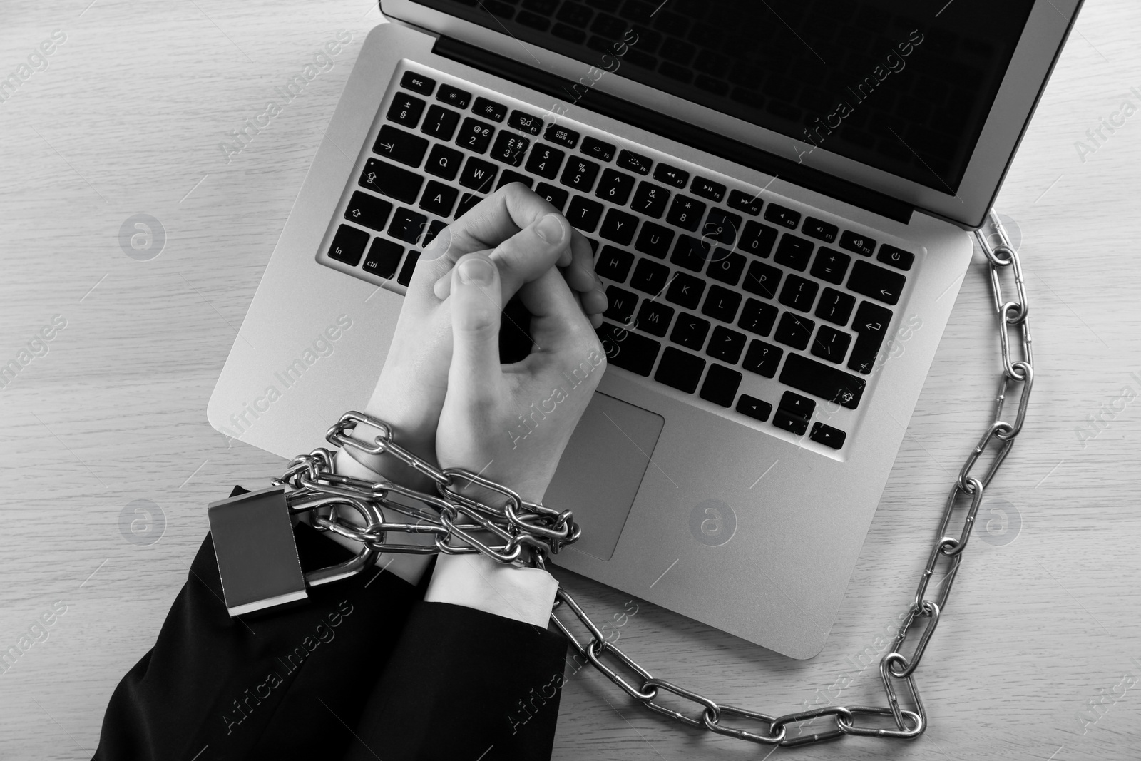 Image of Top view of woman with chained hands and laptop at wooden table, black and white effect. Internet addiction