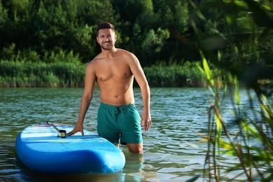 Photo of Man standing near SUP board in river water on sunny day