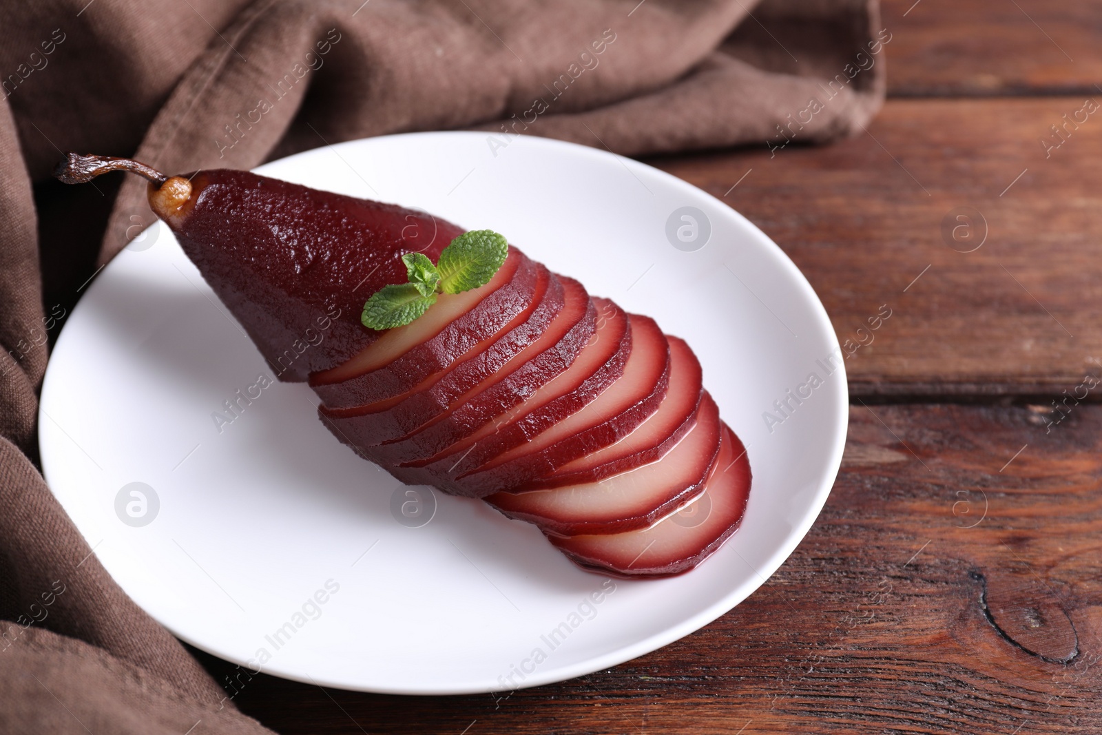 Photo of Tasty red wine poached pear on wooden table, closeup