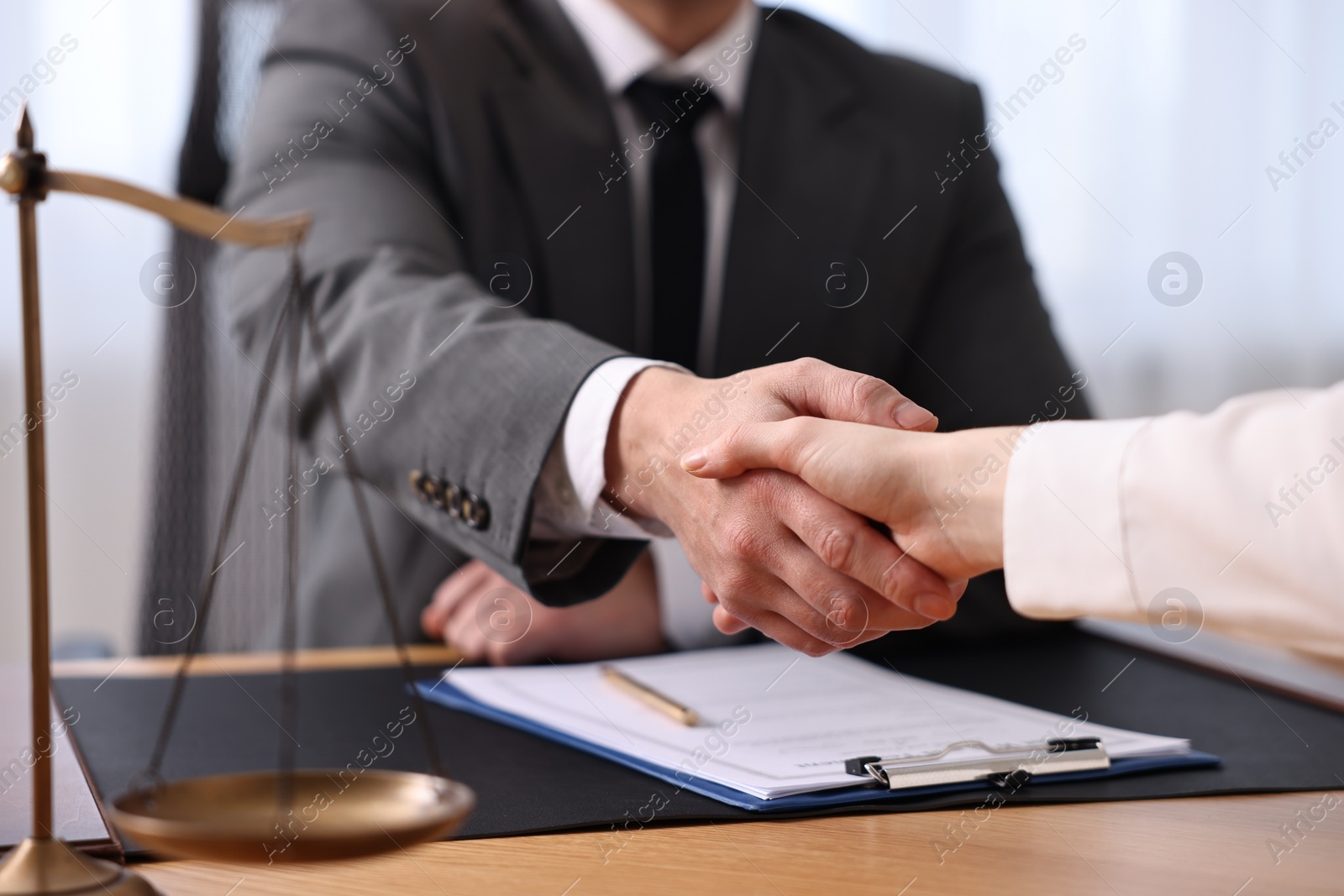 Photo of Notary shaking hands with client at wooden table in office, closeup