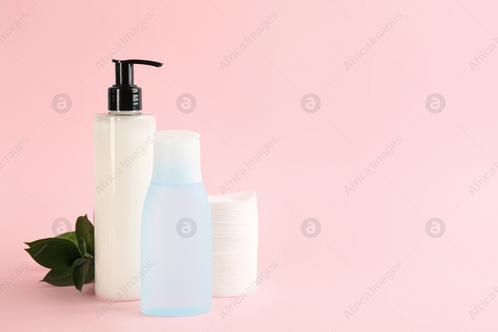 Photo of Cotton pads, leaves and makeup removal products on pink background. Space for text