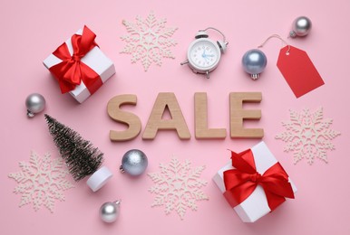 Photo of Word Sale made of wooden letters, gift boxes, alarm clock and Christmas decorations on pink background, flat lay