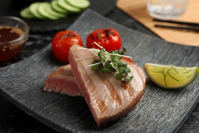 Photo of Pieces of delicious tuna with microgreens, lime and tomatoes on table, closeup